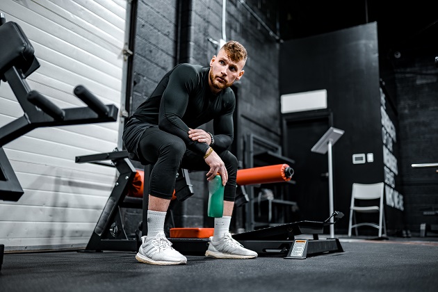 Bărbat musculos, îmbrăcat în negru, în timp ce stă pe unul dintre aparatele din sala de fitness.