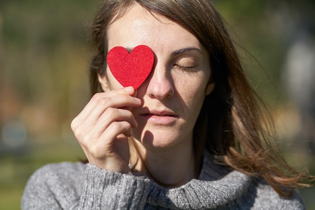 Femeie care își acoperă ochiul drept cu o inimă roșie de carton.