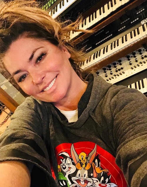 Shania Twain fericită, înconjurată de instrumente muzicale, într-o bluză cu personaje din desene animate.