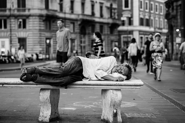 Om al străzii care doarme pe o bancă, îmbrăcat în haine rupte și murdare.