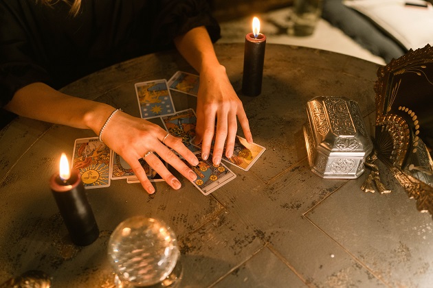 Femeie care ghicește în cărțile de tarot așezate pe o masă, alături de alte elemente care au legătură cu magia.