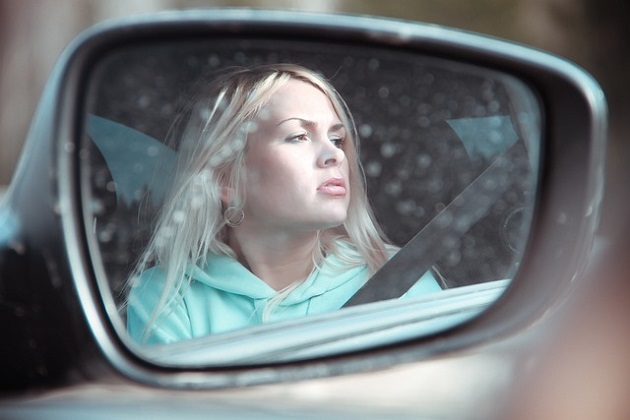Femeie bondă care privește peisajul de pe geamul mașinii, dar care are o atitudine gânditoare