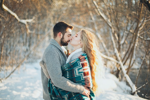 Îndrăgostiți care se îmbrățișează și se sărută într-un cadru de iarnă.