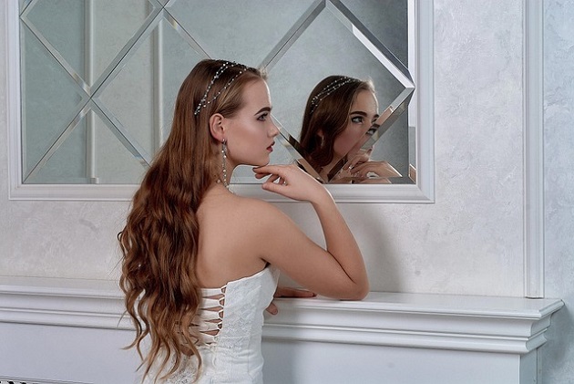 Mireasă încrezătoare care stă în fața oglinzii și privește într-o parte.