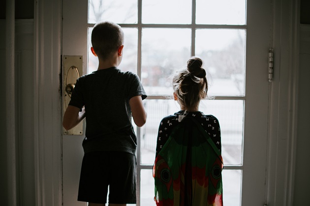Frate și soră care stau lângă ușă, privind peisajul prin geam