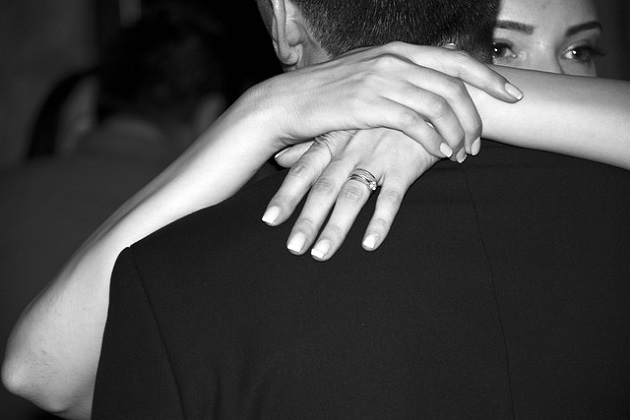 Imagine alb negru cu o femeie care își îmbrățișează partenerul cu emoție, în timp ce el poartă un sacou negru.