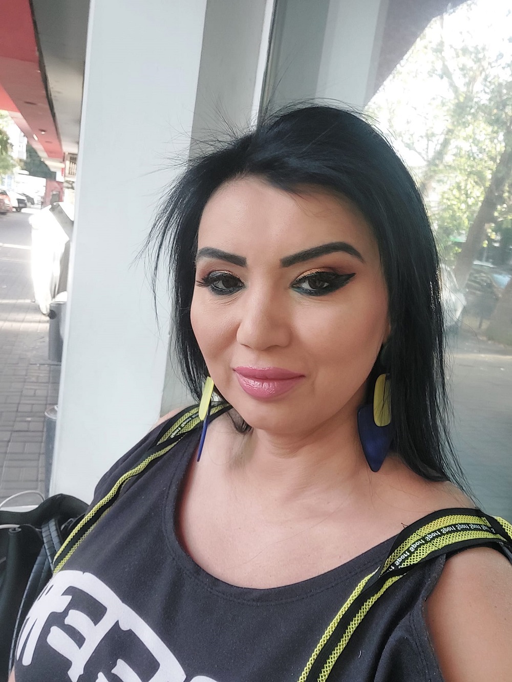 Adriana Bahmuțeanu într-un maiou negru, purtând o pereche de cercei colorați.