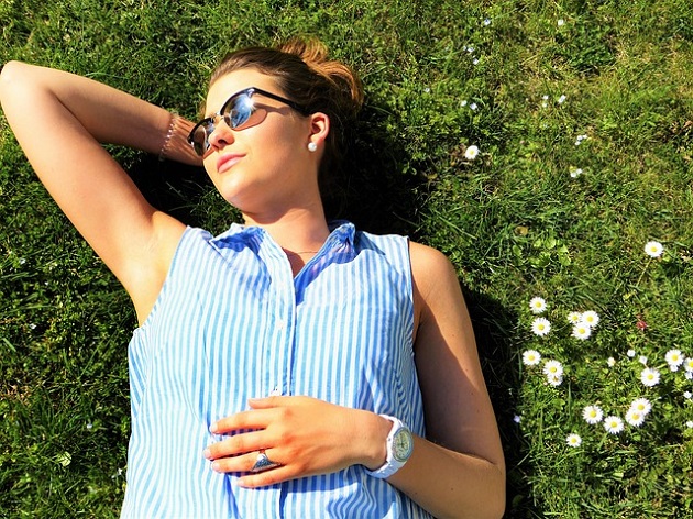 Femeie cu ochelari de soare care stă întinsă și relaxată pe iarbă