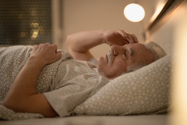 Bătrân care stă în pat, ținându-se cu mâna de cap, fiindcă suferă de insomnie