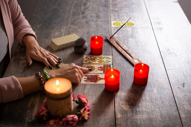 Femeie cu unghii lungi și negre care ghicește în cărțile de Tarot, așezate pe o masă lângă lumânări și un bețișor parfumat.