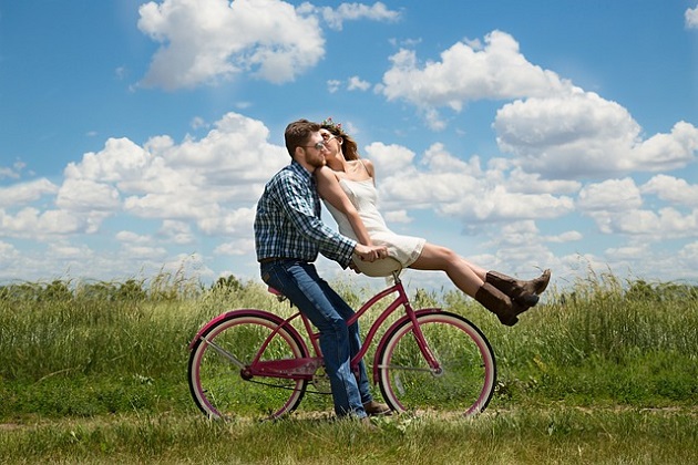 Bărbat care își plimbă iubita pe cadrul de la bicicletă, în timp ce ea îl sărută pe obraz