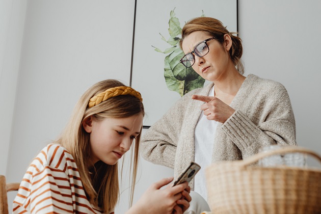 Mamă care își ceartă fiica adolescentă în timp ce ea este concentrată la conținutul vizionat pe telefon