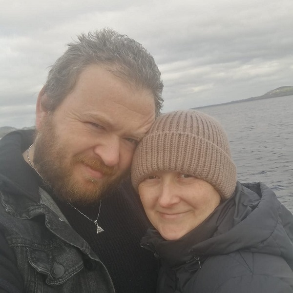 Dave McLoughlin și partenera sa Michelle Crowe, îmbrățișați pe malul mării pe timp de iarnă și îmbrăcați gros