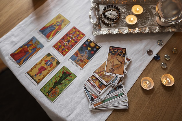 Cărți de tarot așezate pe o masă alături de alte elemente ce țin de magia neagră - lumânări, mătănii