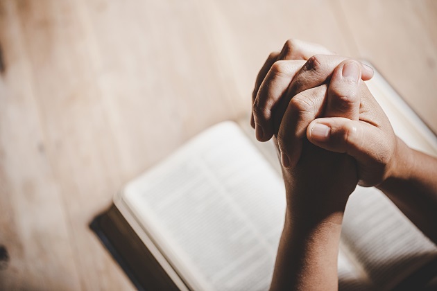 Mâinile unei persoane care se roagă cu o biblie în față