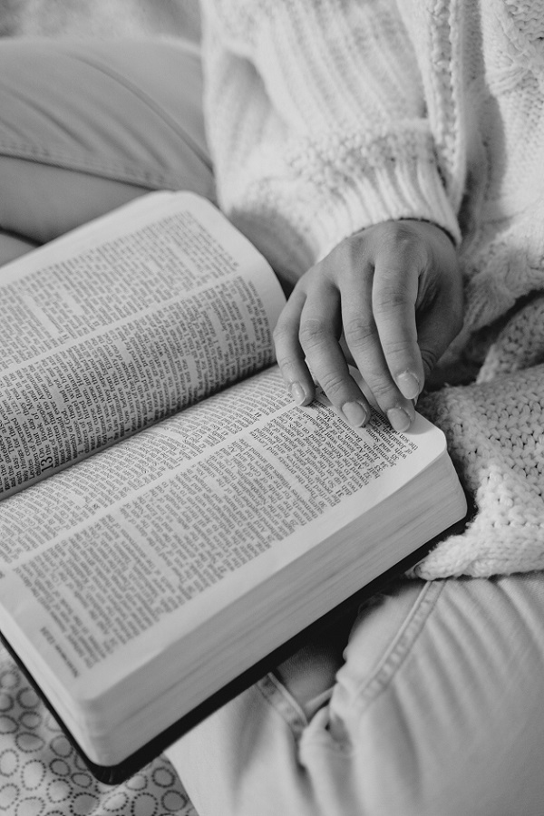 Femeie care stă cu picioarele încrucișate și citește Biblia.