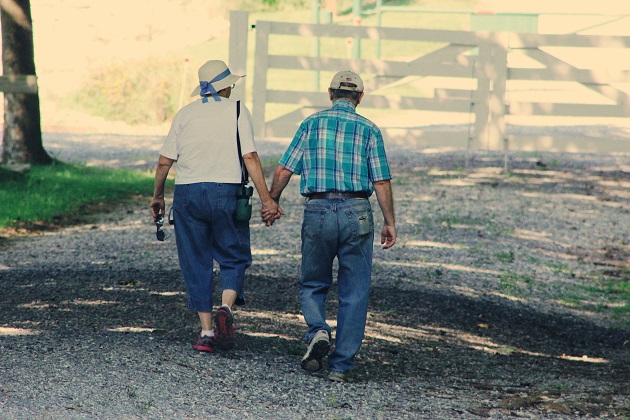 Doi oameni în vârstă care se plimbă și se țin de mână.