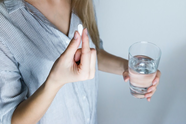Femeie care se pregătește să ia o pastilă, în timp ce ține și paharul cu apă într-o mână.