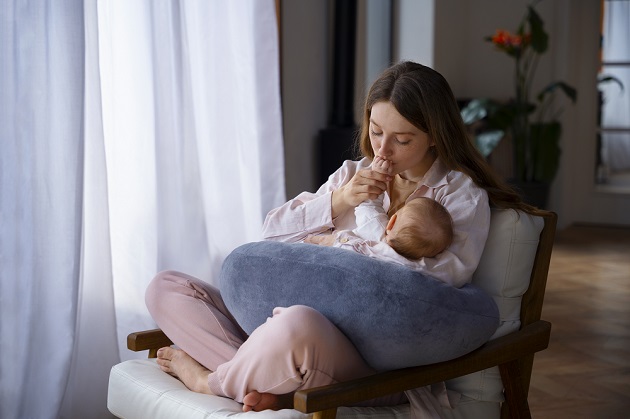 Tânără mamă care își ține bebelușul în brațe și îl sărută pe mână