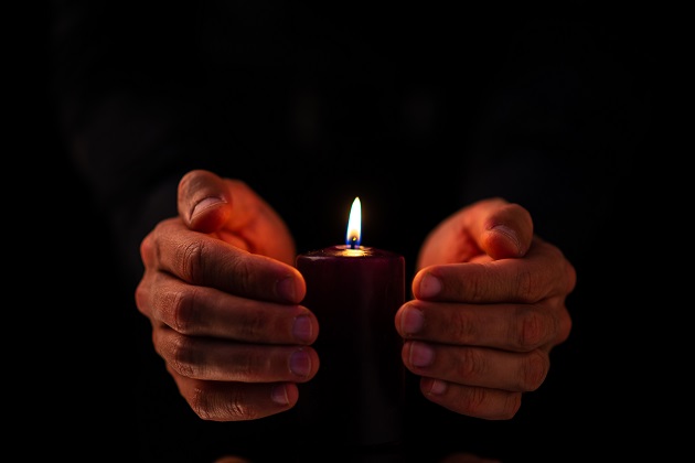 Persoană care protejează flacăra lumânării cu propriile mâini