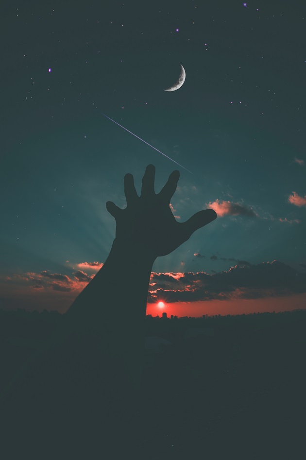 Persoană care ridică mâna spre cer la apus, în timp ce se zărește și luna