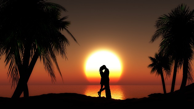 Siluetele unor îndrăgostiți care se îmbrățișează la apus, printre palmieri