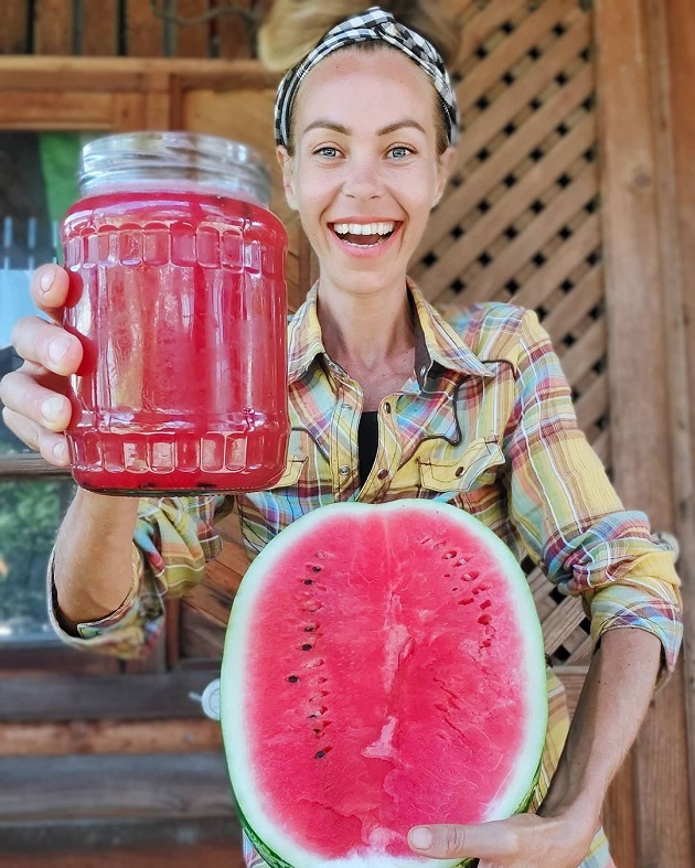 Zhanna Samsonova ținând într-o mână jumătate de pepene și în cealaltă un borcan cu suc de pepene