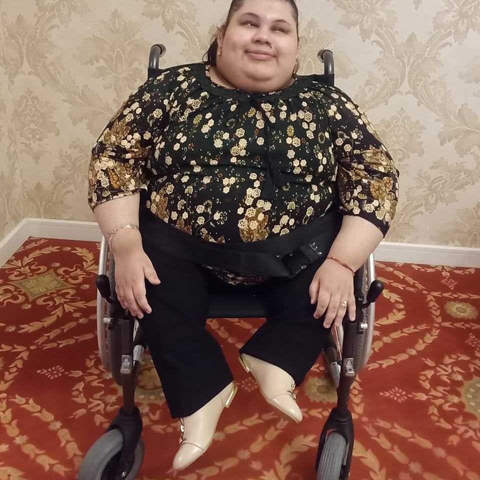 Alexandra Marghioala îmbrăcată într-o bluză cu flori, stând în scaunul ei cu rotile