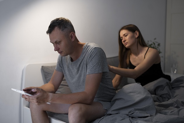 Femeie care încearcă să atragă atenția partenerului în timp ce el navighează pe internet și nu o bagă în seamă