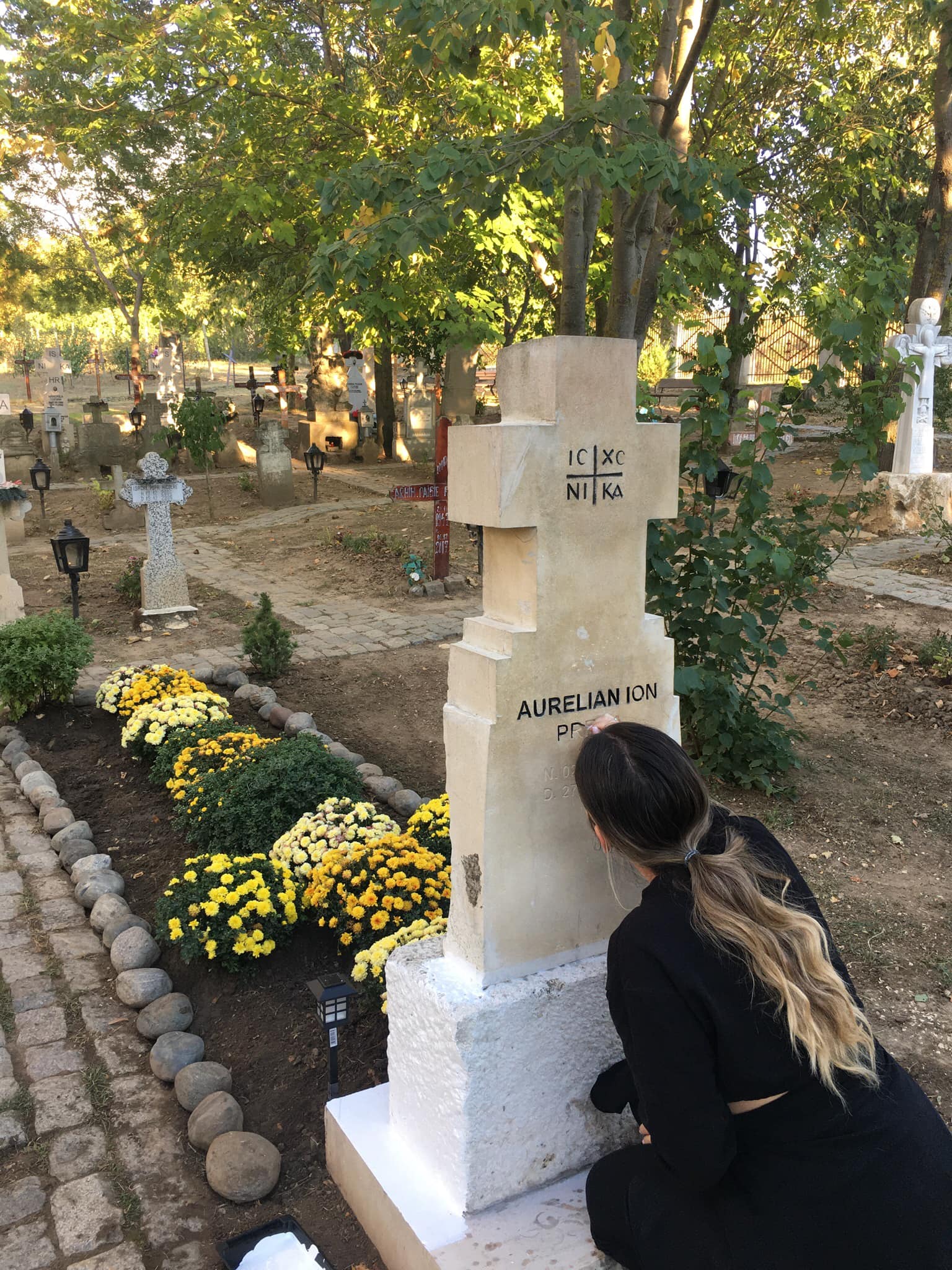 Anamaria Rosa Preda conturează literele de pe crucea de la mormântul tatălui său