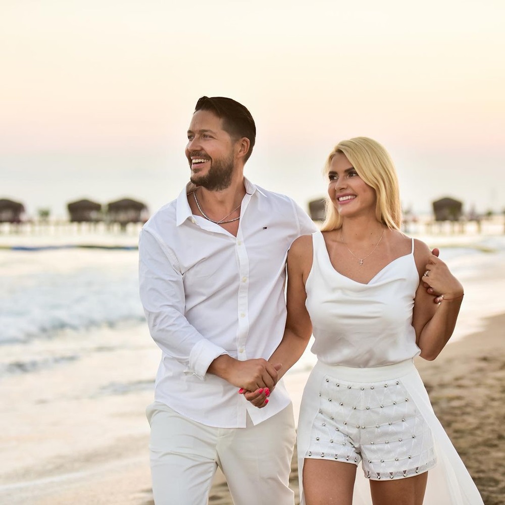 Jorge și soția sa fericiți pe plajă, îmbrăcați amândoi în alb, sărbătorind 10 ani de căsnicie