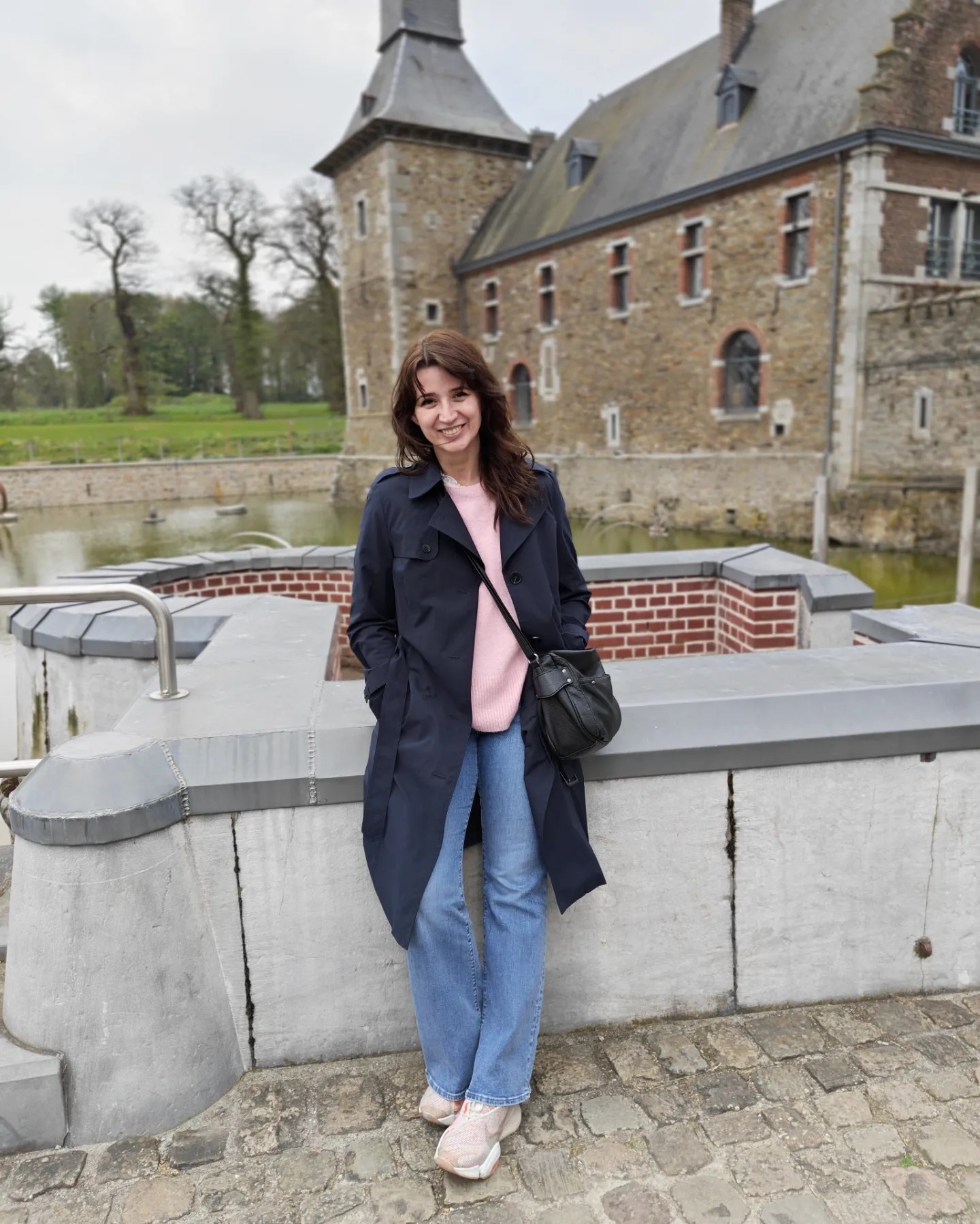 Sanda Nicola într-o pereche de blugi largi, un pulover roz pal și un trenci bleumarin la Castelul Jehay din Belgia.