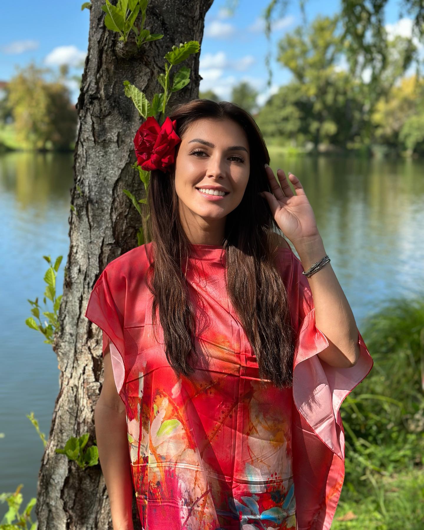 Ilinca Vandici pe malul unui lac, îmbrăcată în roșu, cu un trandafir roșu la ureche