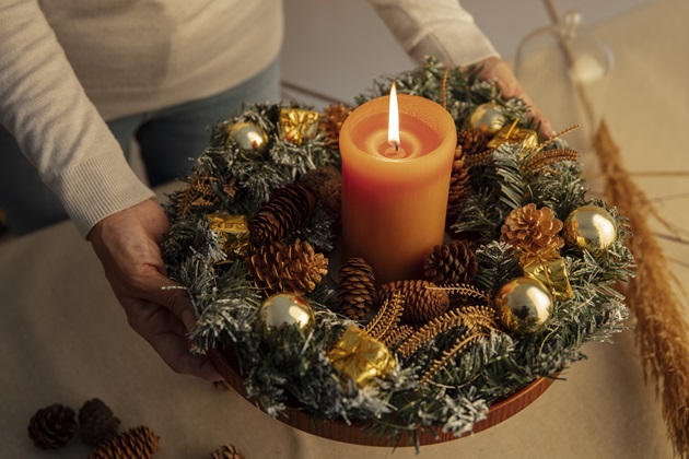 Aranjament pentru masa de Crăciun, făcut din crengi de brad, conuri  și globuri, în mijlocul căruia se află o lumânare portocalie aprinsă