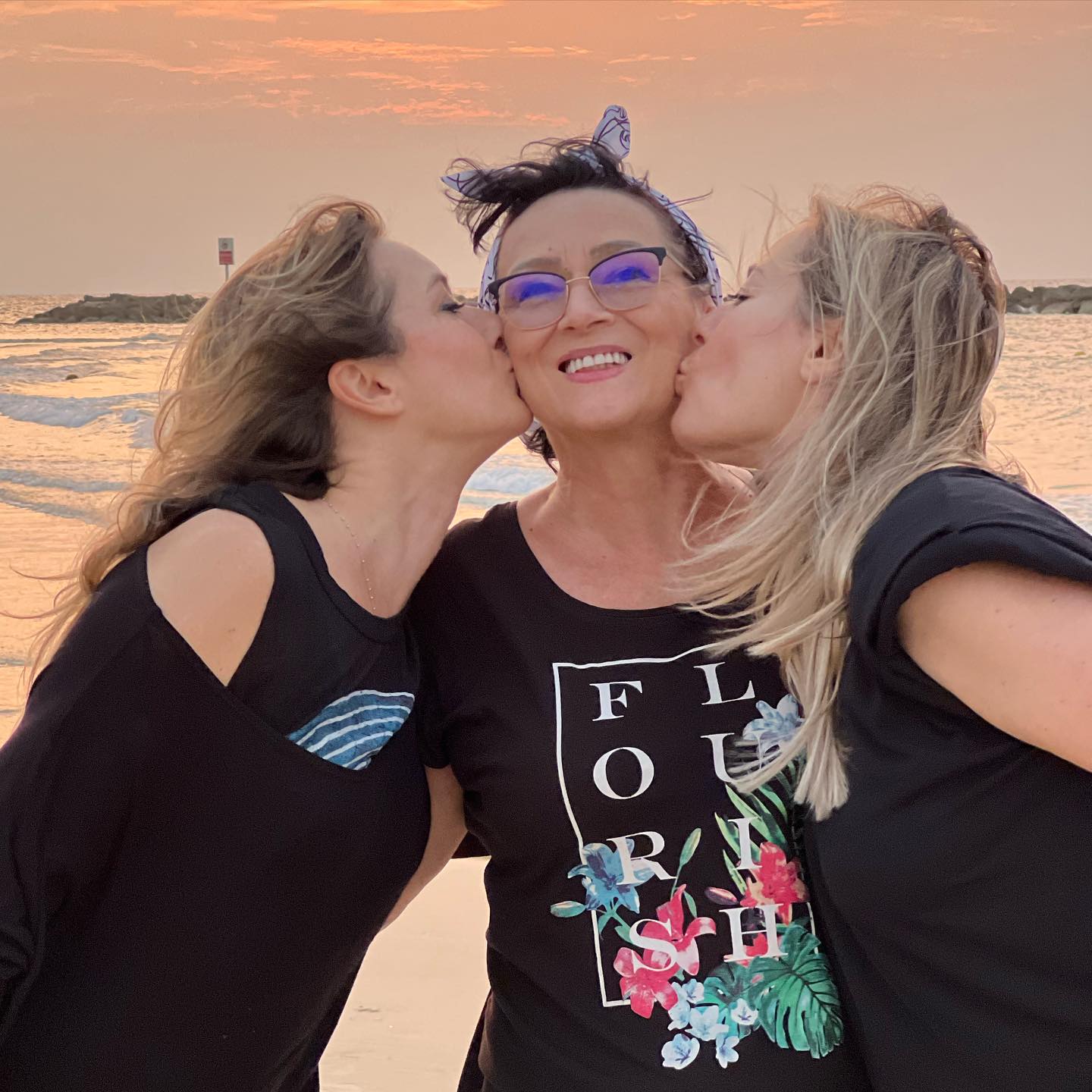 Laura și Alina Cosoi sărutându-și mama pe obraz la malul mării