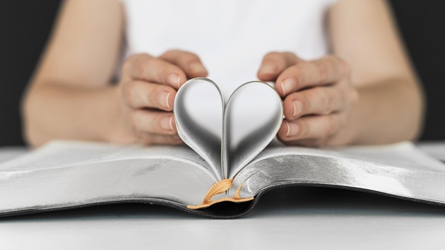 Femeie îmbrăcată în alb, care formează o inimă din paginile Bibliei
