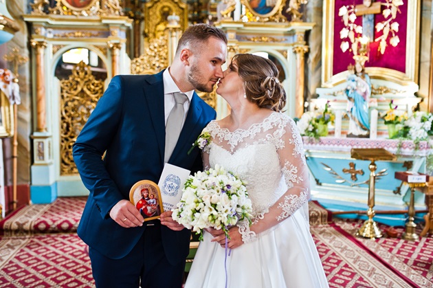 Mireasă în rochie albă care își sărută soțul în Biserică, după Taina Căsătoriei
