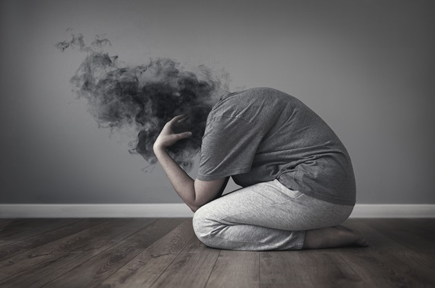 Persoană anxioasă, care stă ghemuită pe podea și are mintea încețoșată de gânduri negre