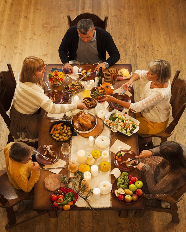 Familie care stă la o masă plină cu mâncăruri alese, în zi de sărbătoare