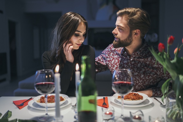 Parteneri apropiați în timpul unei cine romantice, unde masa este decorată cu lumânări și flori