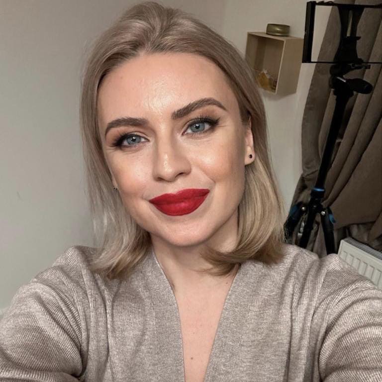 Andreea Liptak îmbrăcată într-un pulover bej, dată cu ruj roșu pe buze