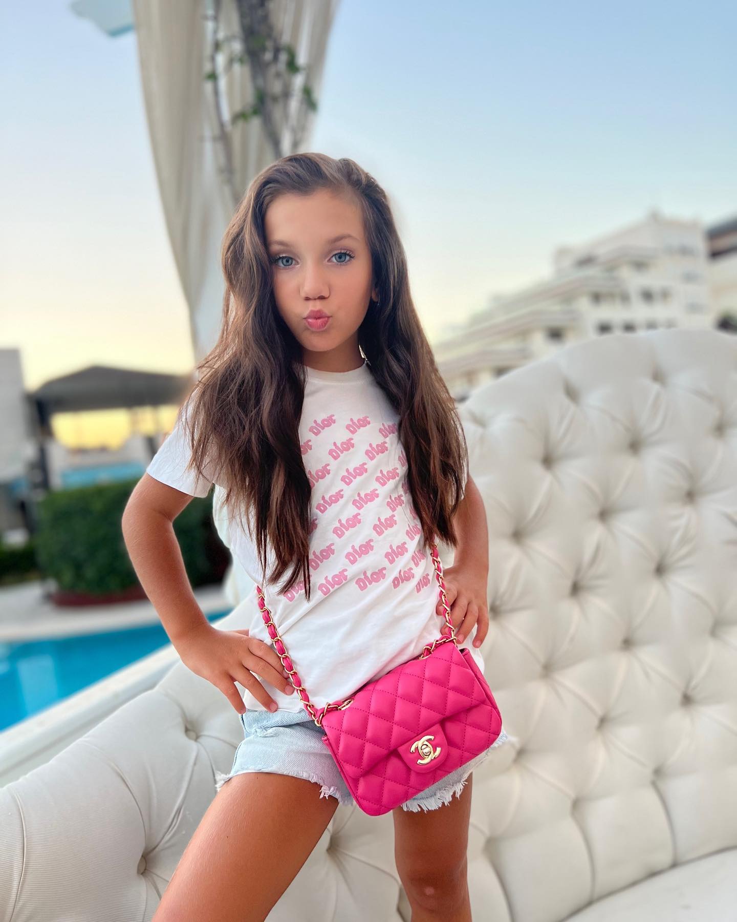Rebecca, fiica Andreei Tonciu, îmbrăcată într-un tricou alb și pantaloni scurți de blugi, ținută accesorizată de o geantă roz bombon