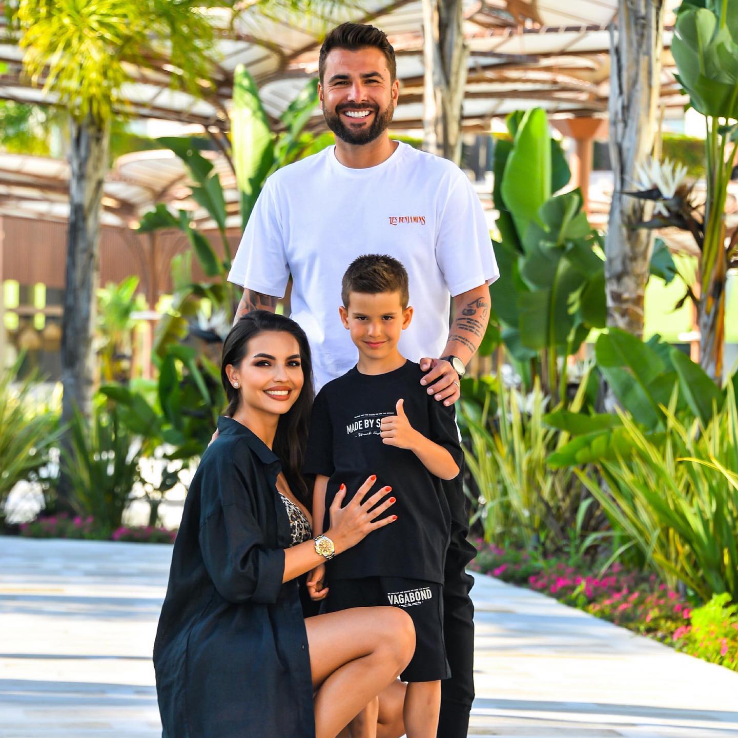 Adrian Mutu, Sandra Mutu și fiul lor Tiago, zâmbitori și îmbrăcați asorat, pe o alee înconjurată de verdeață