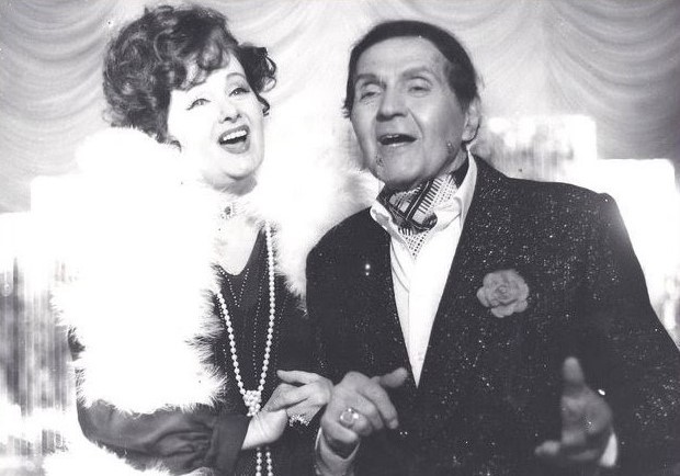 Gică Petrescu pe scenă, cântând alături de Stela Popescu, în timp ce amândoi erau îmbrăcați în haine elegante