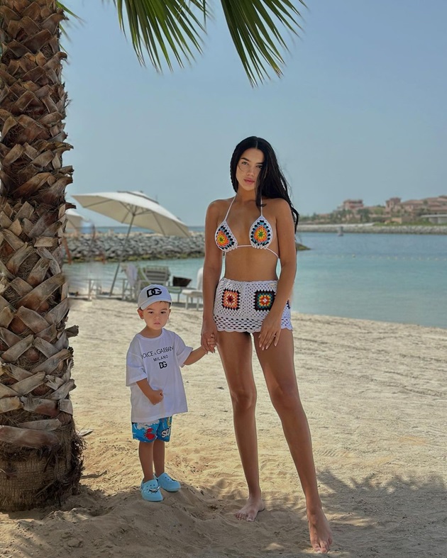 Larisa Udilă în costum de baie, pe plajă, lângă palmieri, alături de fiul ei Milan
