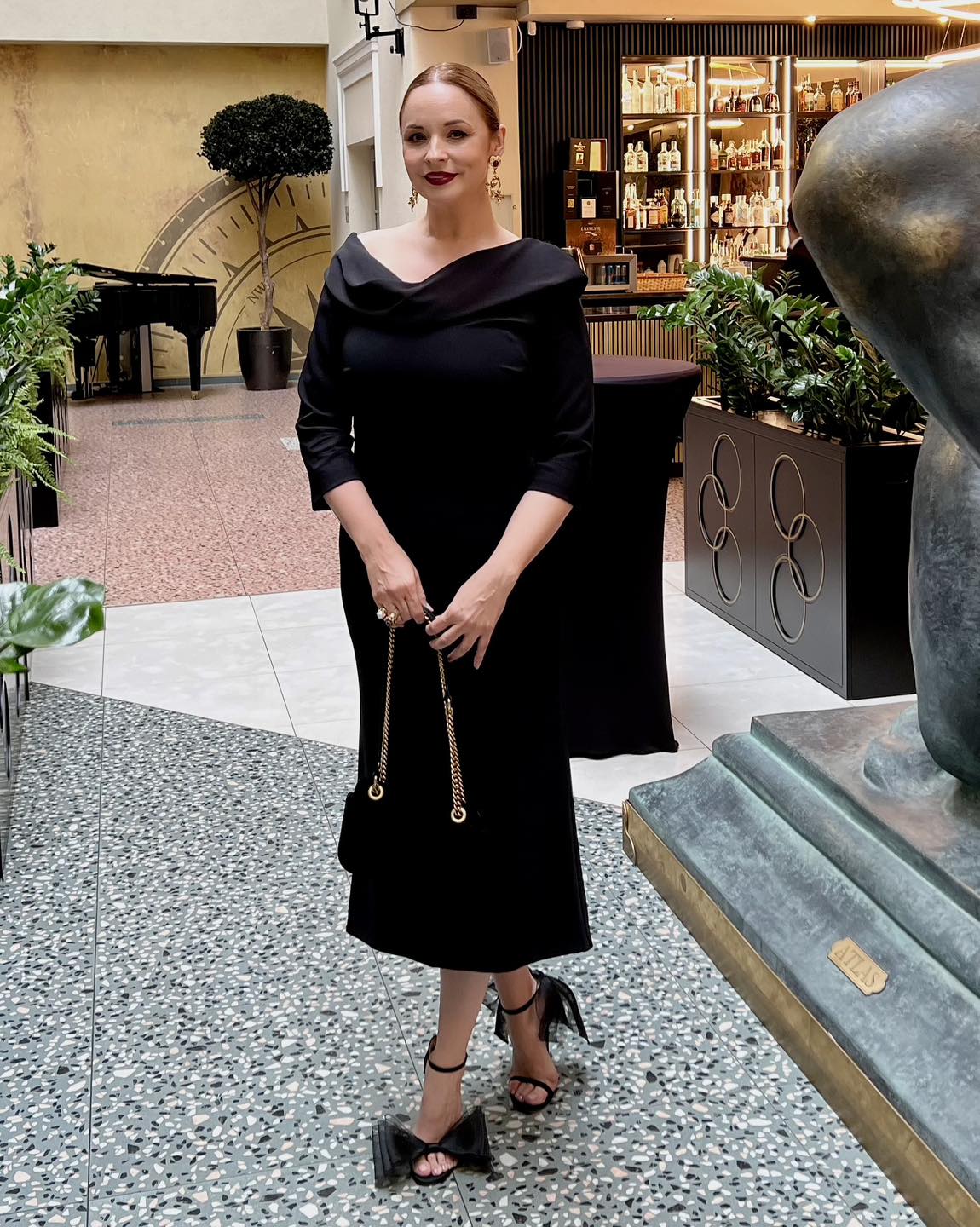 Andreea Marin cu părul prins, îmbrăcată într-o rochie neagră, pe care a asorat-o cu sandale și geantă în aceeași nuanță