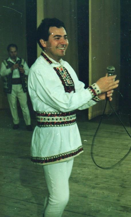 George Rotaru în tinerețe, pe scena Casei de Cultură din Făgăraș, în costum popular, cu microfonul în mână