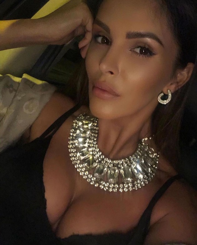 Denisa Nechifor s-a fotografiat într-o lumina slabă, sprijinindu-și capul cu mâna, în timp ce purta la gât și în urechi bijuterii luxoase