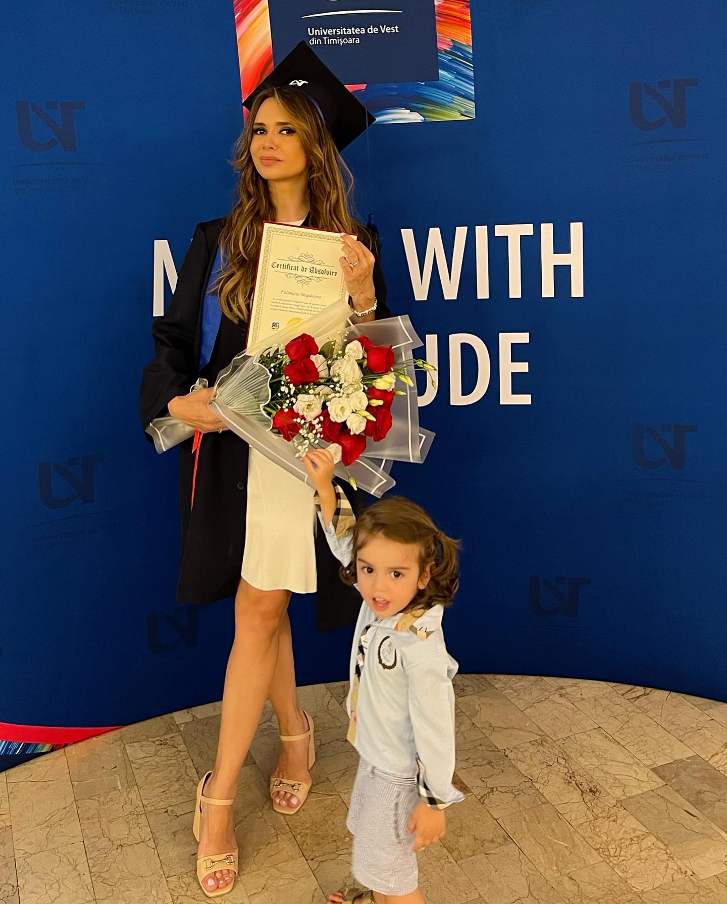 Magda Pălimariu, în ziua absolvirii, ținând într-o mână certificatul de absolvire și în cealaltă un buche de flori de care se ține băiețelul ei, Aksel