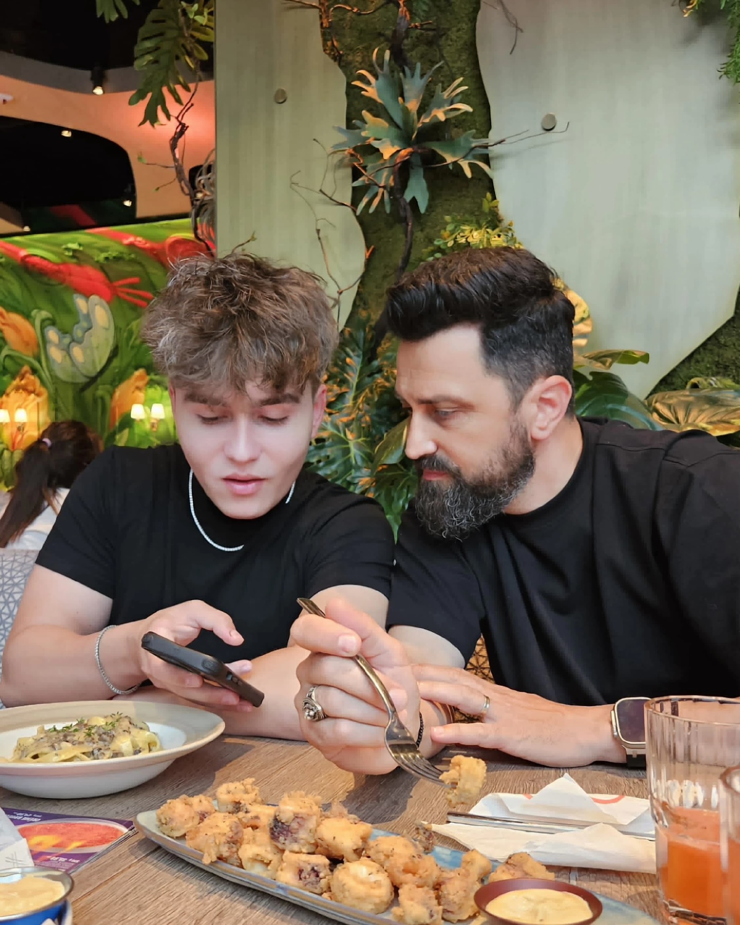 Chef Orlando Zaharia luând masa la restaurant alături de fiul său, Andreas Zaharia, care îi arată ceva pe telefon